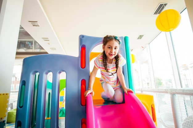 Niña feliz divirtiéndose en un tobogán en el centro de juegos Una niña linda está jugando en el patio de recreo