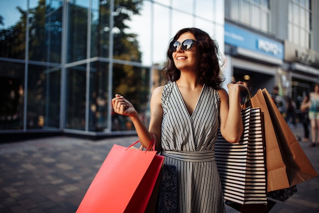 Niña feliz se encuentra cerca de la tienda boutique con algunas bolsas con compras.