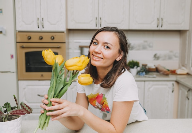 Niña feliz se encuentra en la cocina con un ramo de flores de tulipanes amarillos para el cumpleaños del día de la madre pascua