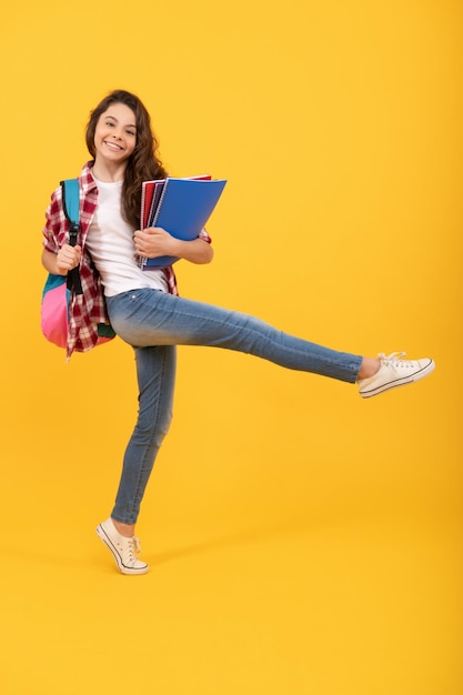 Niña feliz y enérgica que se apresura a ir a la escuela con libros y mochila el 1 de septiembre fondo amarillo Día del conocimiento