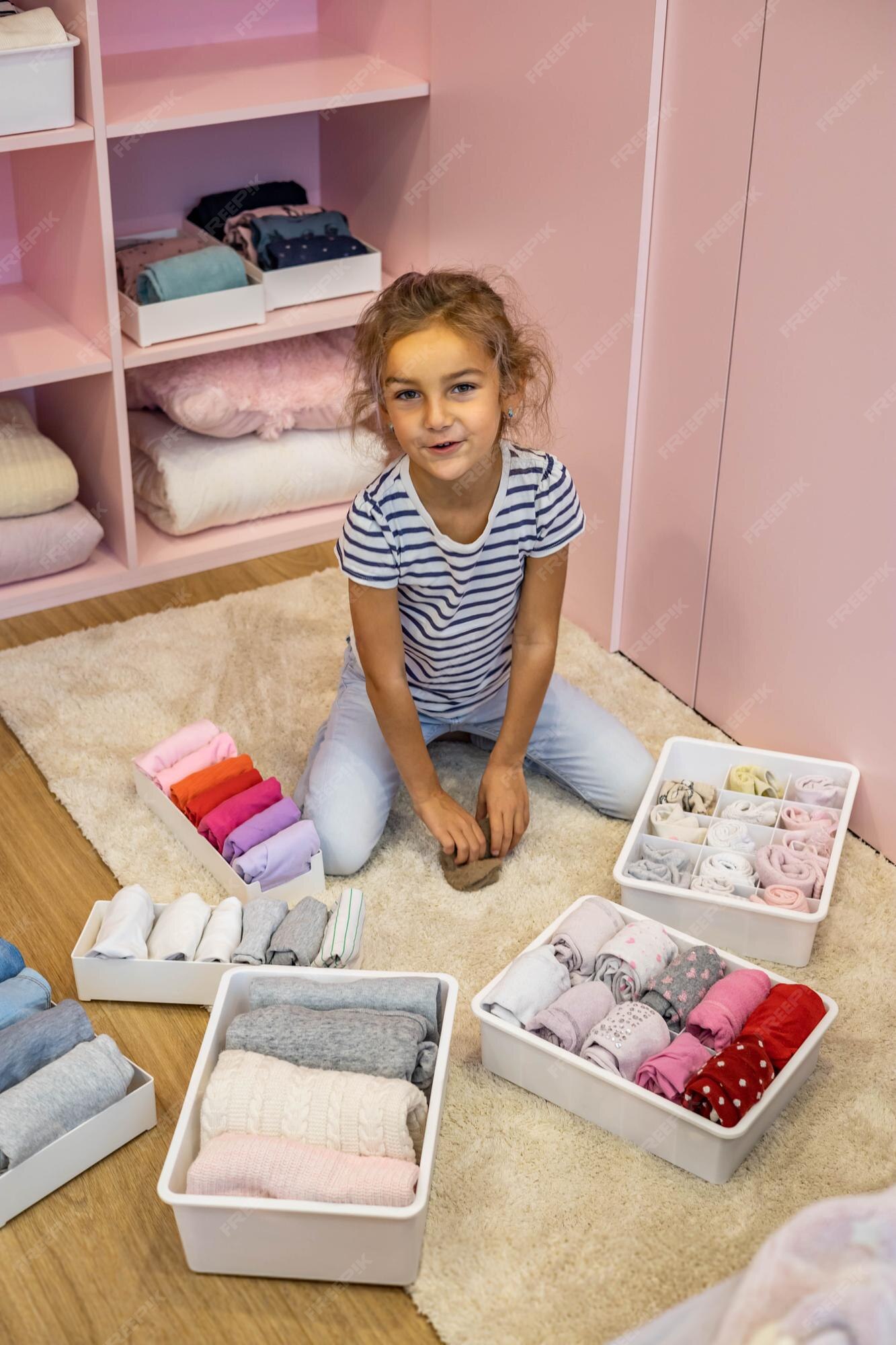 La niña feliz enrolla cuidadosamente la ropa interior y calcetines en una caja de plástico método marie kondo | Foto Premium