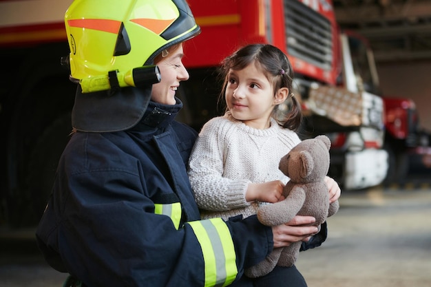 La niña feliz está con una bombera con uniforme protector