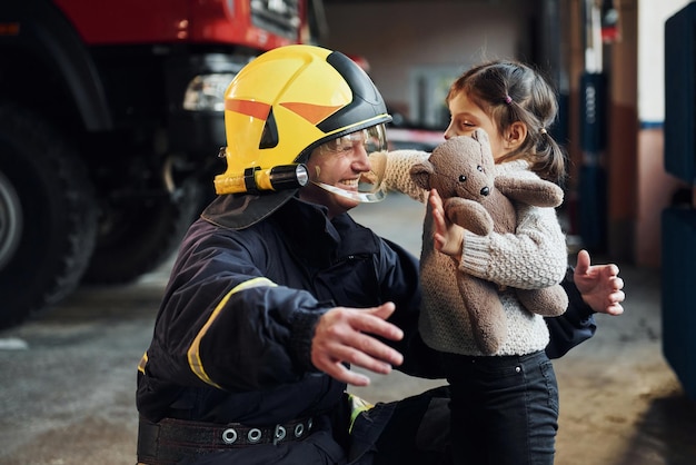 La niña feliz está con un bombero con uniforme protector