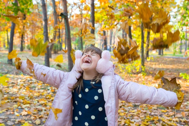 Una niña feliz está jugando con hojas de otoño en el parque en un cálido y soleado día de otoño