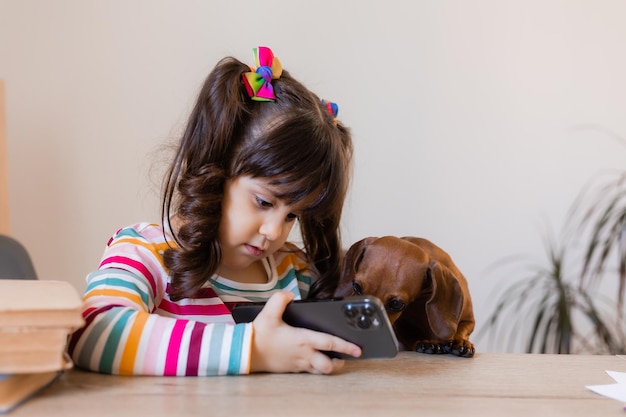 Una niña feliz está mirando el teléfono con un pequeño perro salchicha Educación preescolar Niños y animales