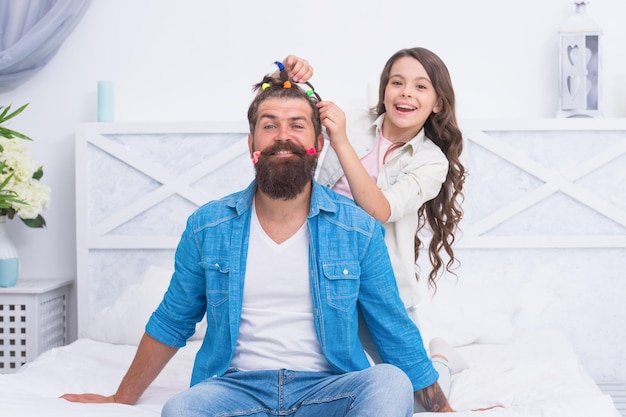 Niña feliz estilista hacer un peinado creativo para un padre barbudo dentro del salón