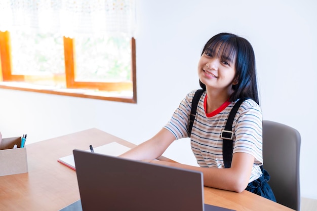 Niña feliz estudiando en casa con laptop, escuela en casa.