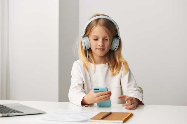 Una niña feliz estudiando en casa usando una computadora portátil para el aprendizaje electrónico está sentada en una mesa con una sonrisa