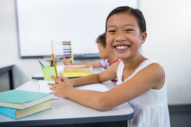 Niña feliz estudiando en el escritorio en el aula