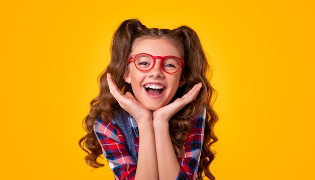 Niña feliz con gafas elegantes y camisa a cuadros tocando la cara y mirando