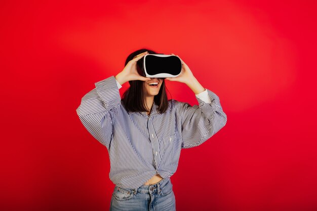 Niña feliz en gafas de realidad virtual. Ella está de pie sobre una superficie roja en el estudio, tiene la experiencia de usar gafas de realidad virtual.