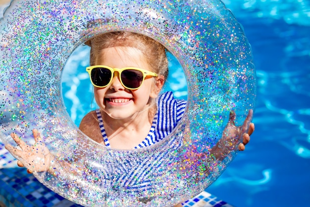 Niña feliz con gafas de sol sostiene un círculo de natación en el espacio de verano para texto