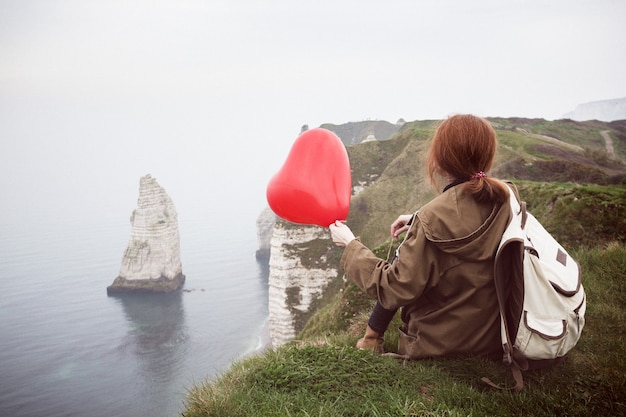 Niña feliz con un globo rojo en forma de corazón en el fondo del paisaje Etretat. Francia