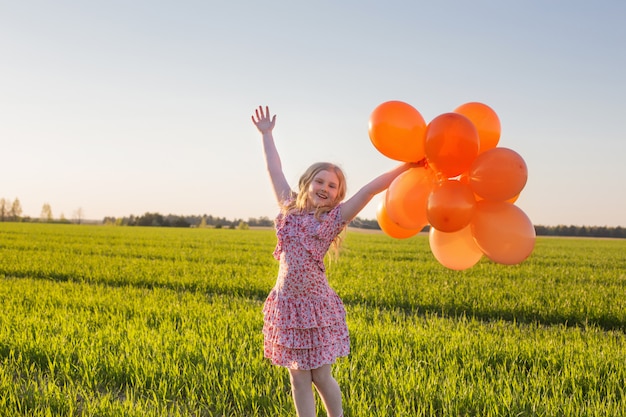 Niña feliz con globos naranjas al aire libre