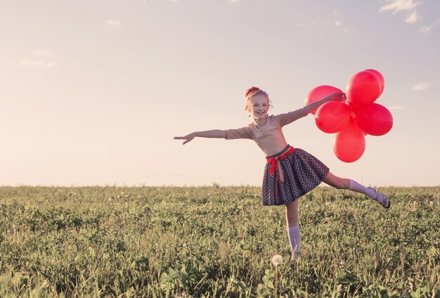 Niña feliz con globos rojos al aire libre