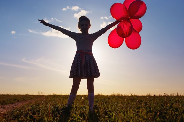 Foto niña feliz con globos rojos al aire libre