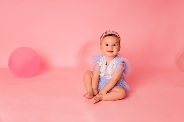 Niña feliz con globos sobre un fondo rosa celebra su primer cumpleaños