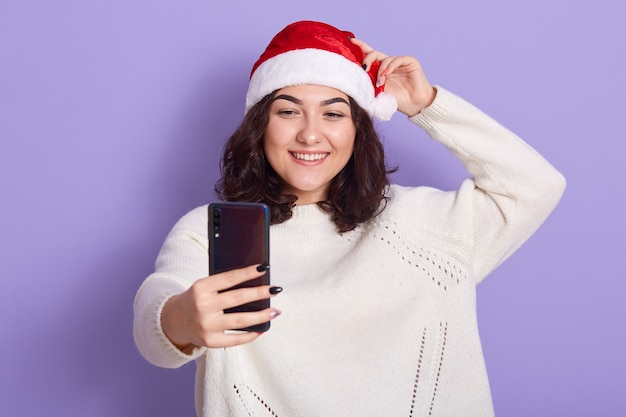 Niña feliz en gorra de Santa Claus con teléfono inteligente en la mano