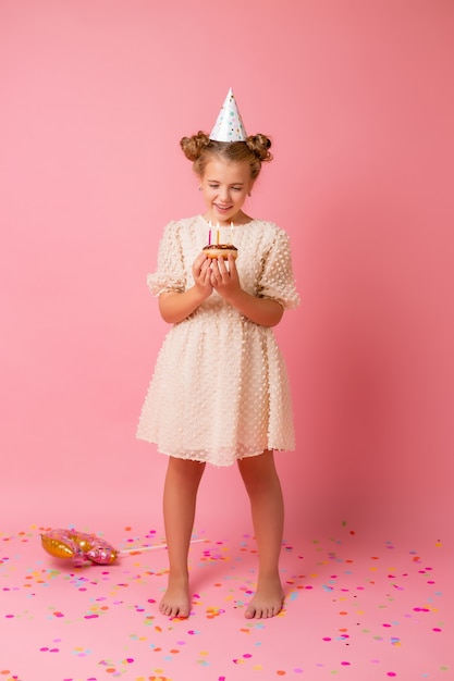 Niña feliz con una gorra para su cumpleaños pide un deseo y sopla velas en un pastel.