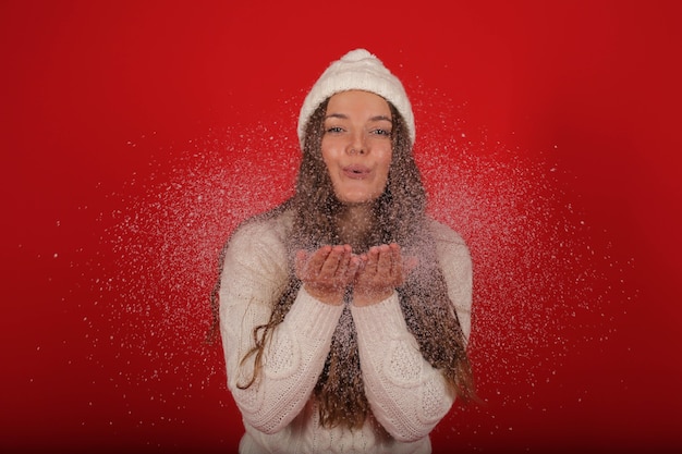 Una niña feliz con un gorro de invierno y un suéter de punto en jeans en el fondo de nieve artificial