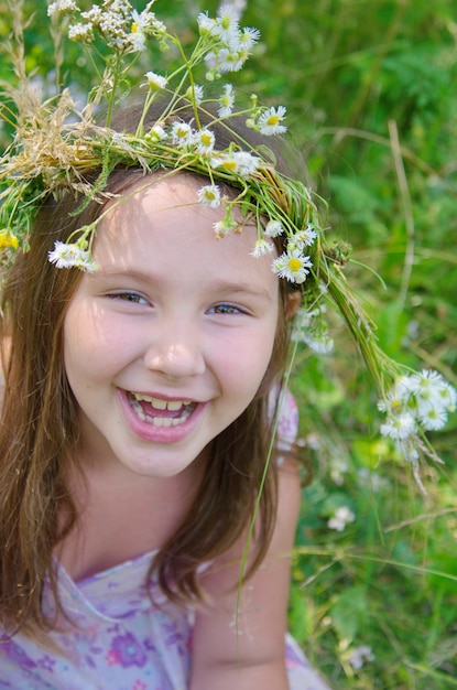 Niña feliz en una guirnalda de flores de campo en el prado