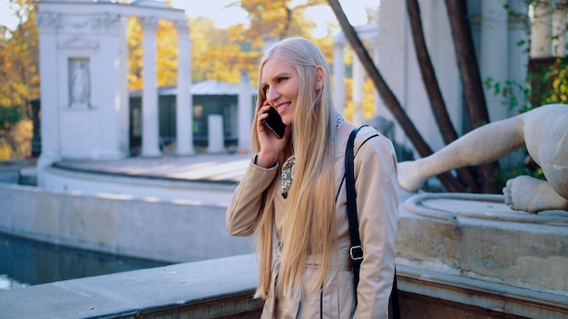 Foto una niña feliz está hablando por un teléfono móvil en el parque otoñal de la ciudad entre el colorido au ...