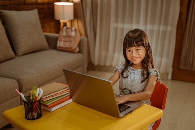 Niña feliz haciendo la tarea usando la computadora portátil