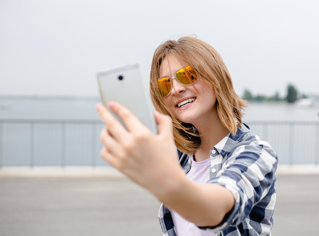 Niña feliz en hipster haciendo selfie en teléfono.