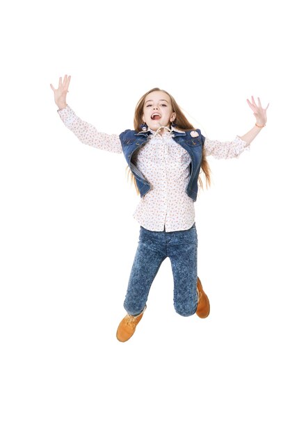 Niña feliz en jeans saltando sobre fondo blanco.