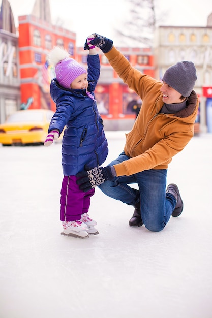 Niña feliz con joven padre divertirse en pista de patinaje