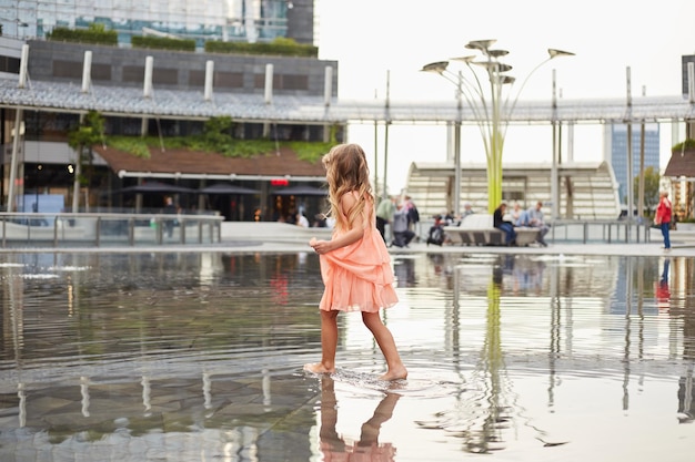 Niña feliz juega con agua en una fuente en la plaza