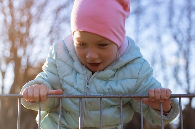 Una niña feliz juega escalando la cerca de hierro en la calle