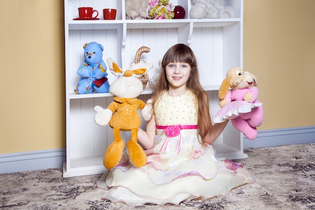 Niña feliz juega con juguetes en su habitación, sonriendo y mirando a cámara. Tiro del estudio.