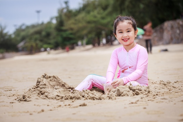 Niña feliz jugando arena en una playa tropical Campamento de verano