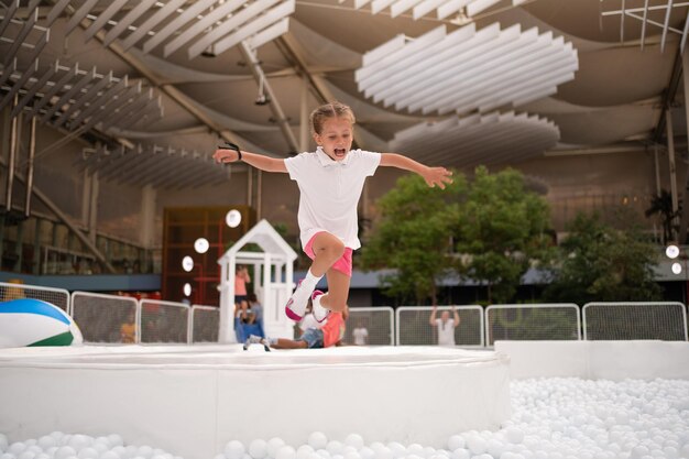 Niña feliz jugando con bolas de plástico blancas en el parque de atracciones para niños