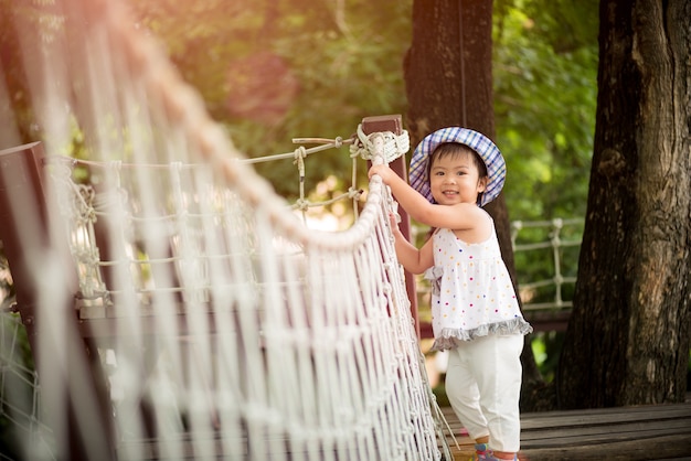 Niña feliz jugando escalada en el puente de cuerda en el jardín