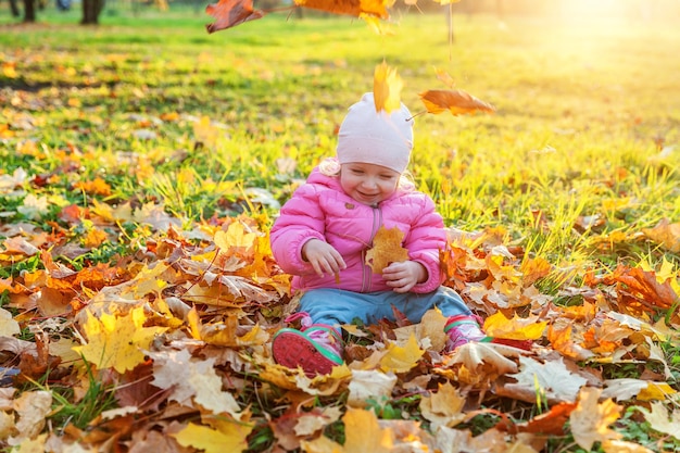 Niña feliz jugando bajo las hojas amarillas que caen en el hermoso parque de otoño en la naturaleza camina al aire libre