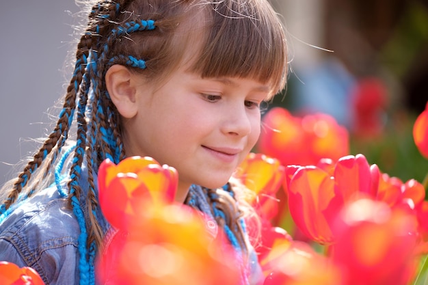 Niña feliz jugando en el jardín de verano disfrutando del dulce aroma de las flores de tulipán rojo en un día soleado