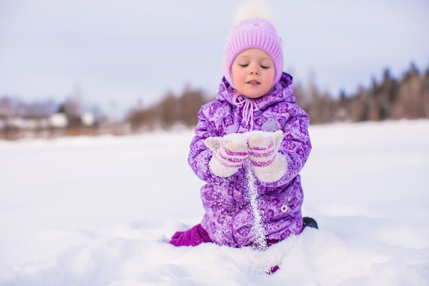 Niña feliz jugando con nieve en un día soleado de invierno