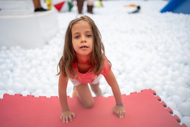 Niña feliz jugando piscina de bolas de plástico blanco en el parque de atracciones