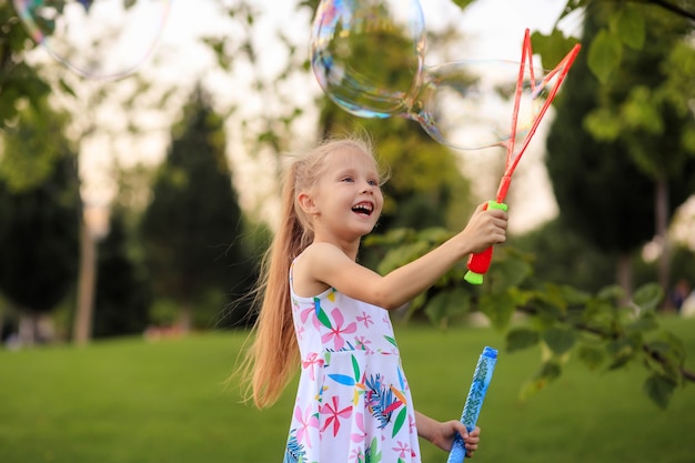 Niña feliz jugando con pompas de jabón de verano en el parque.