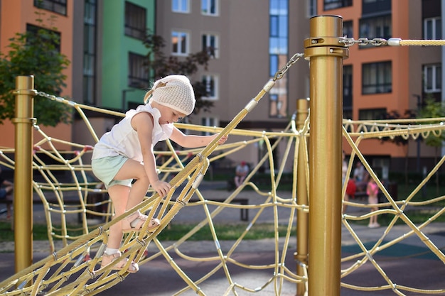 Una niña feliz jugando en una red de cuerdas en el patio de recreo Patio moderno Recreación activa en la ciudad