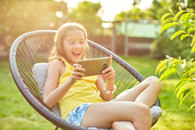 Niña feliz jugando en el teléfono móvil en el parque al aire libre