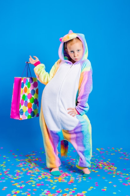 Una niña feliz en un kigurumi de unicornio sostiene una bolsa de regalo