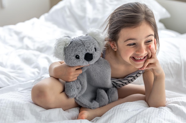 Niña feliz con koala de peluche en la cama