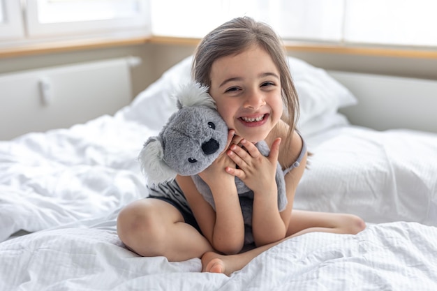 Niña feliz con koala de peluche en la cama