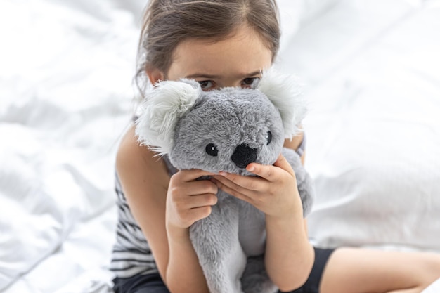 Niña feliz con koala de peluche en la cama