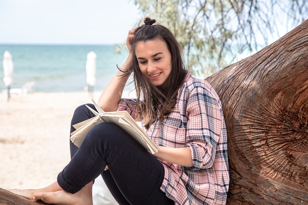 Una niña feliz lee un libro en un árbol. La persona se abstrae de todo. El concepto de relajación y tranquilidad.