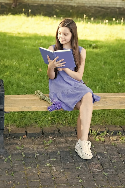 Niña feliz leyendo un libro al aire libre día soleado concepto de hobby inteligente