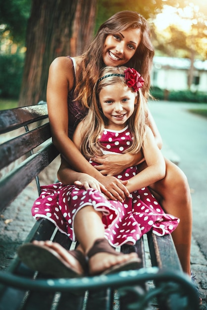 Una niña feliz y linda y su madre están jugando en el parque. Se están abrazando y sonriendo.